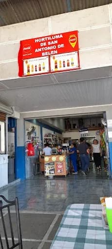 The entrance of the Hortiluma store in San Antonio de Belén, with its sign above the door and customers at the counter inside.